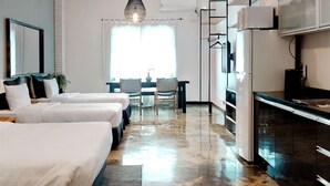 Une chambre d’hôtel avec deux lits, une table à manger avec des chaises, un coin cuisine et une grande fenêtre avec des rideaux.