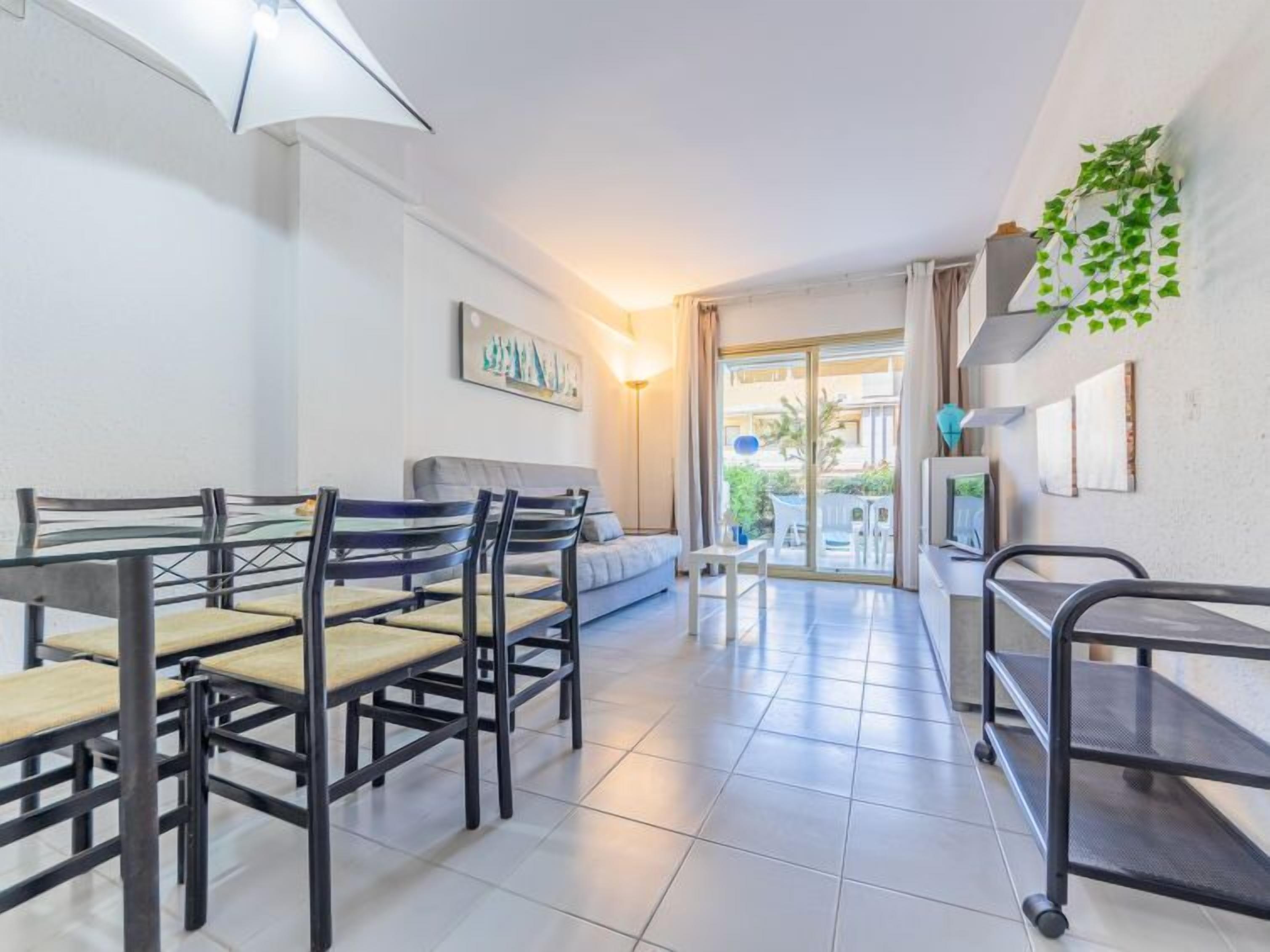 Una sala de estar moderna con sofá, mesa de comedor y sillas. Hay un ventanal corredero que da a un área exterior.