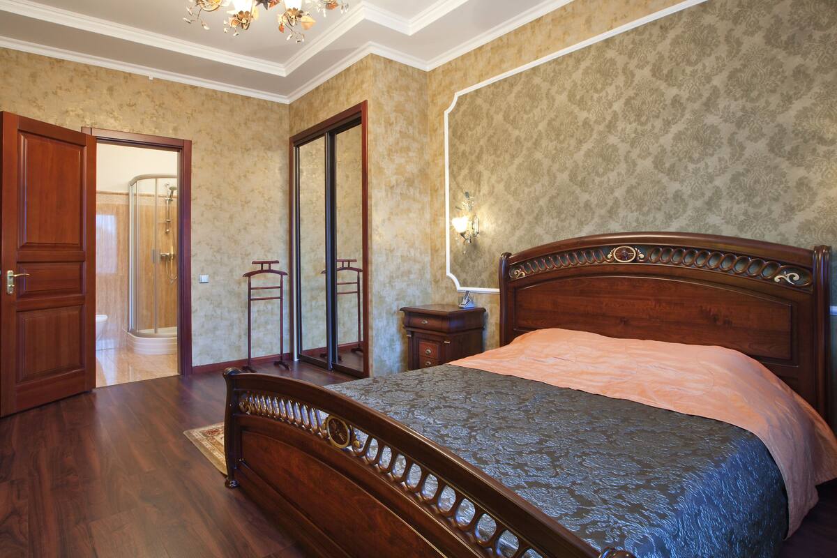 Une chambre à coucher avec un lit en bois, une table de chevet, un miroir et une porte donnant sur une salle de bain.