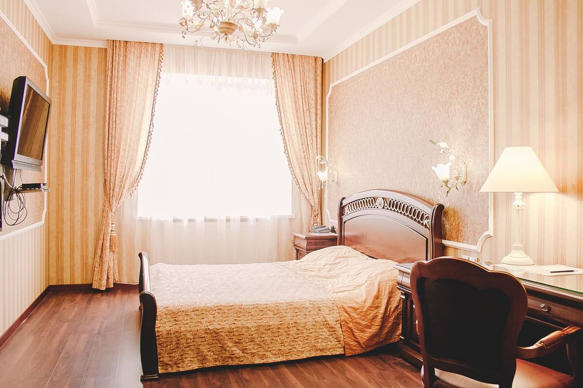 Une chambre d’hôtel avec un lit, un bureau avec une lampe, une chaise, une télévision et des rideaux.