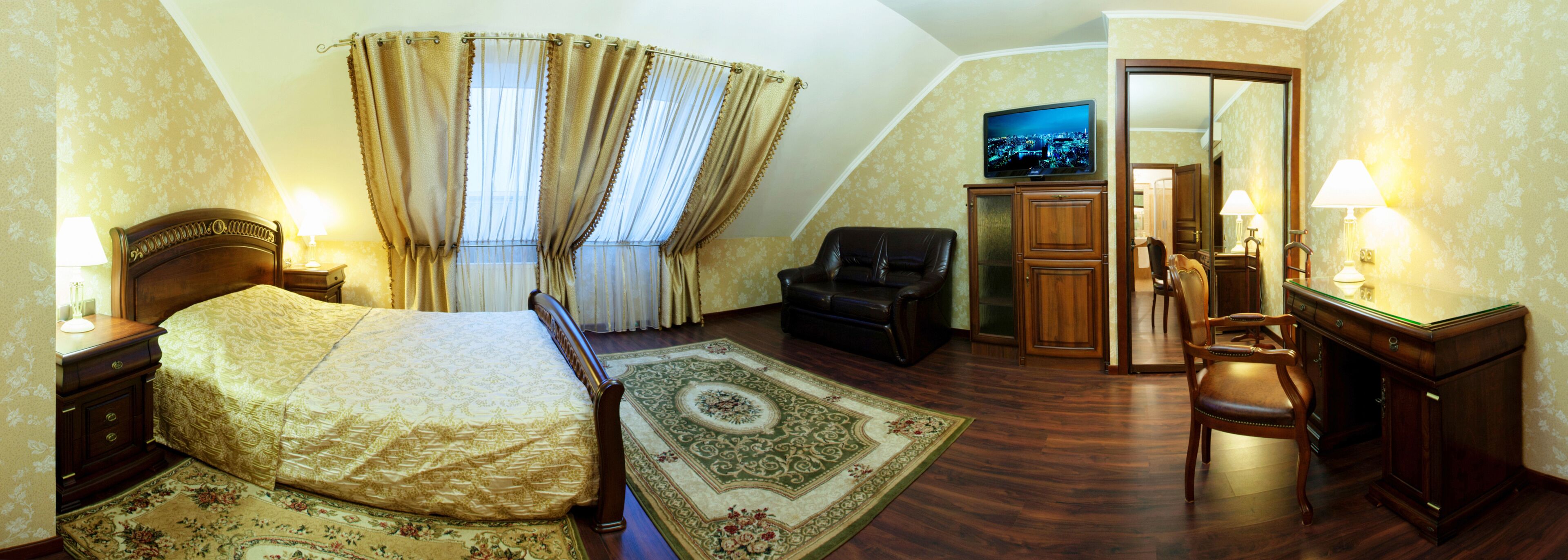 A bedroom with a bed, a chair, a desk, a television, and a mirror.