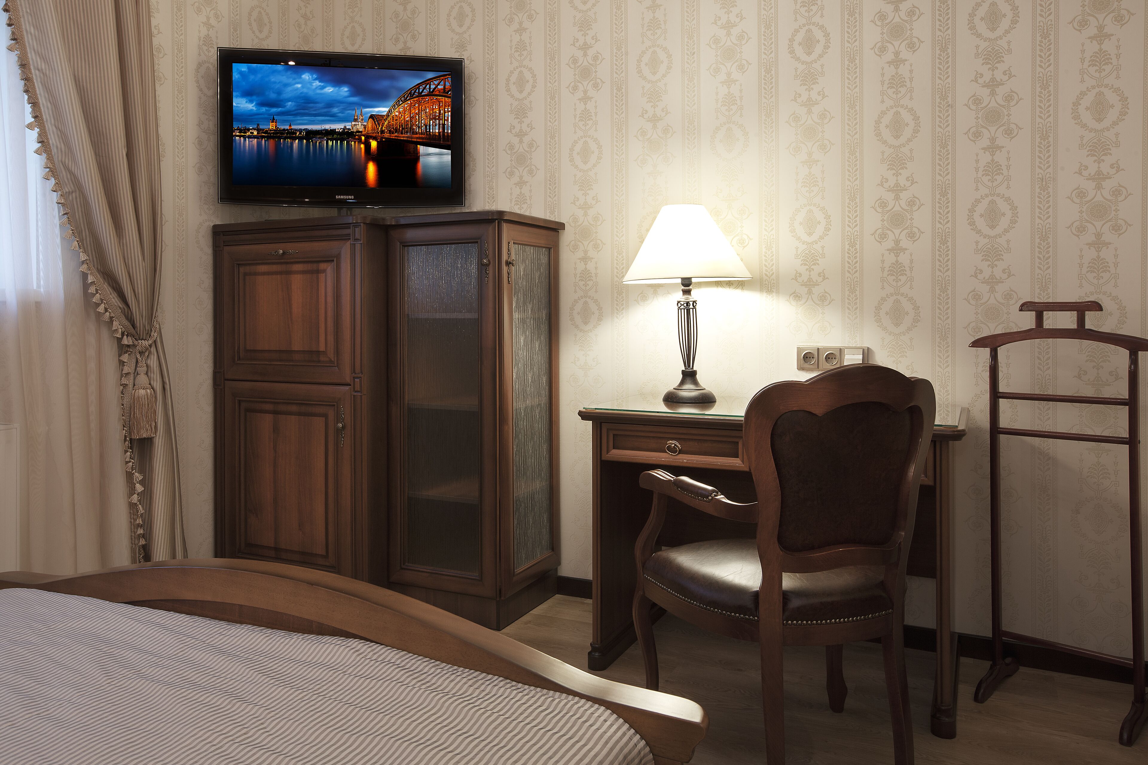 Habitació d'hotel amb llit, escriptori amb cadira, televisió penjada sobre l'escriptori i làmpada sobre l'escriptori.