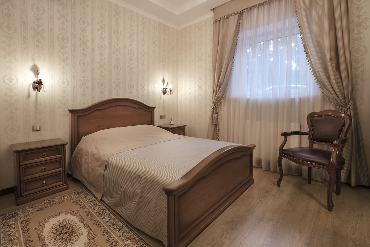 Une chambre à coucher avec un lit en bois, des tables de chevet, une chaise et un papier peint à motifs.