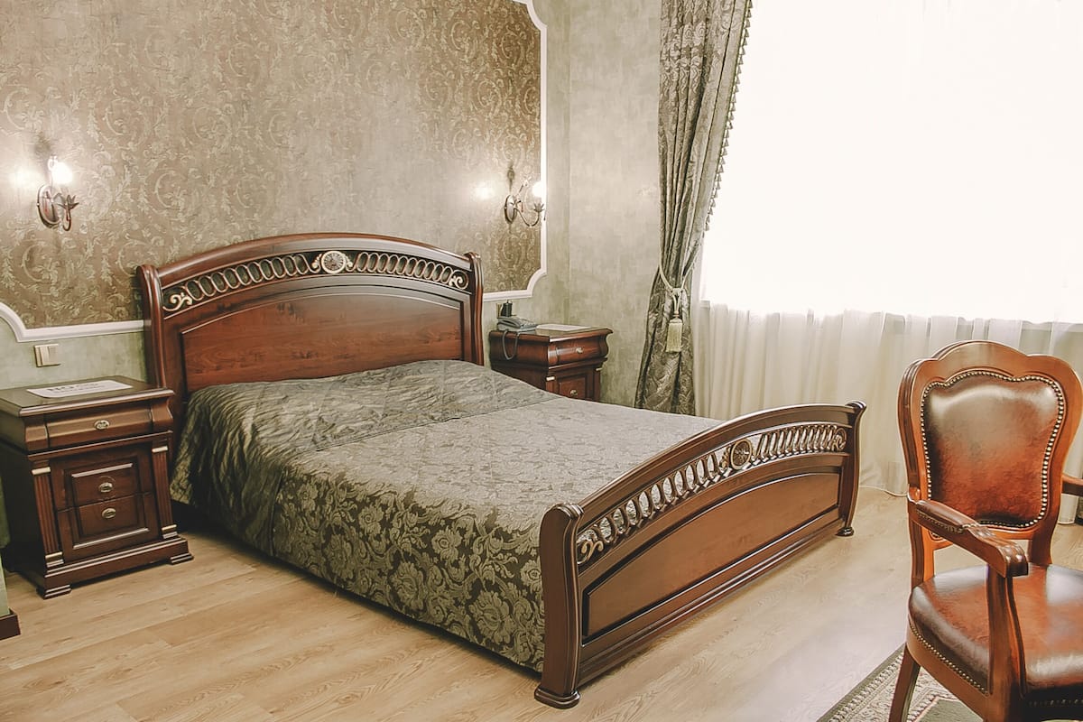 Une chambre à coucher avec un lit en bois, une table de chevet, une chaise et un miroir au mur.