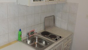 Une petite cuisine avec des meubles blancs, un évier à deux bacs, une cuisinière et une poubelle.
