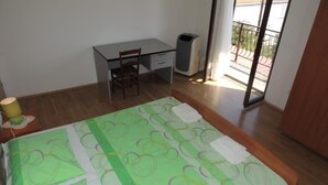 Une chambre à coucher comprenant un lit, un bureau, une chaise, une poubelle et un balcon.