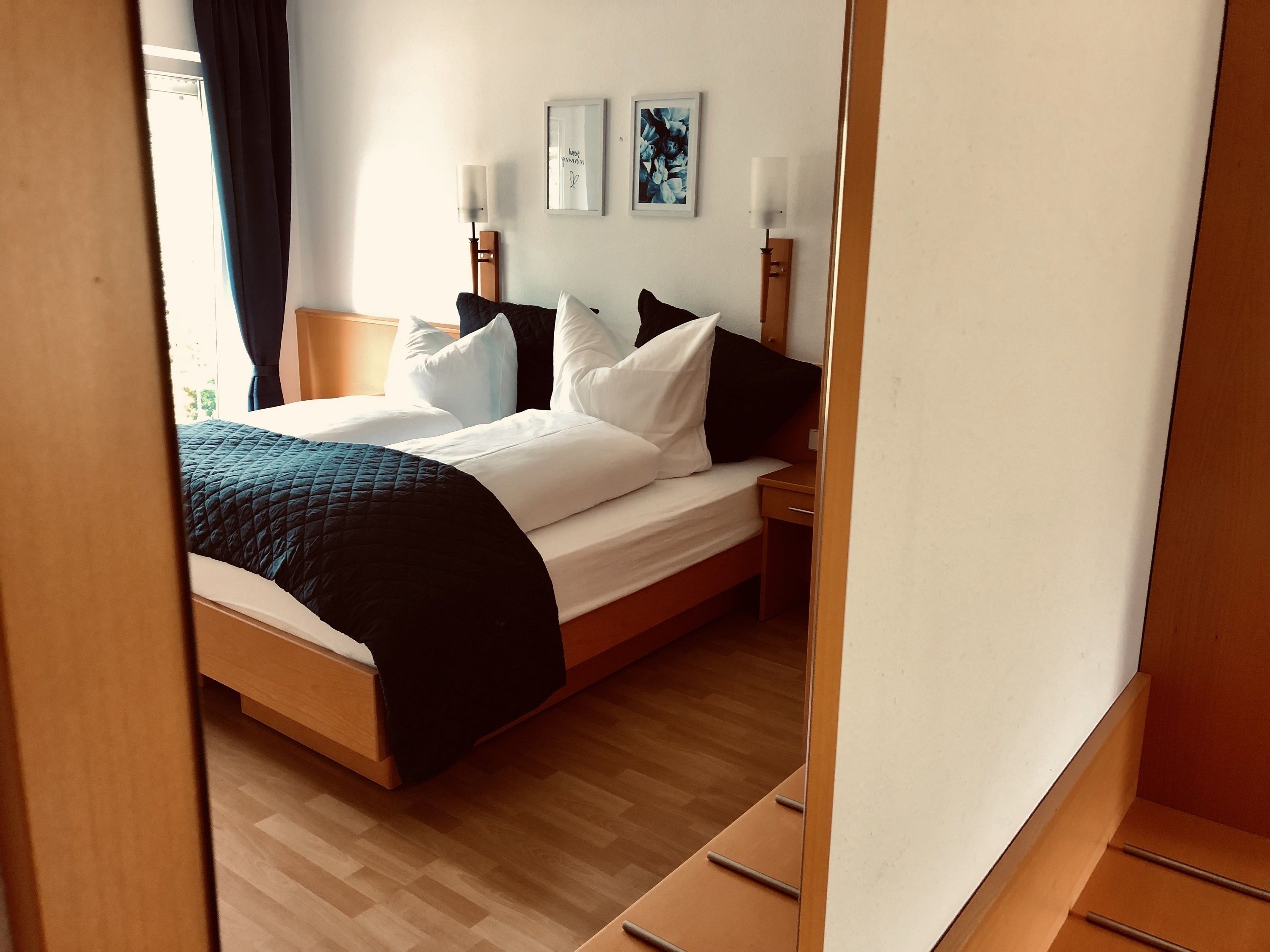 Una cama bien hecha con ropa de cama blanca y negra, un cabecero de madera y una mesita de noche con una lámpara.