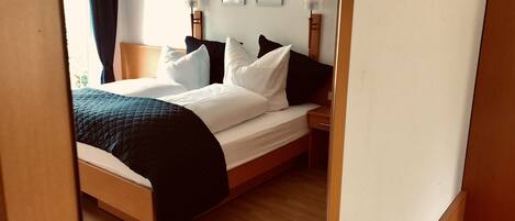 Una cama bien hecha con ropa de cama blanca y negra, un cabecero de madera y una mesita de noche con una lámpara.