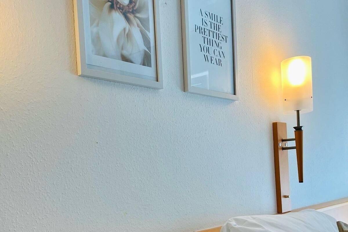 Une chambre d’hôtel avec un lit, deux tableaux encadrés au mur et une lampe fixée au mur.
