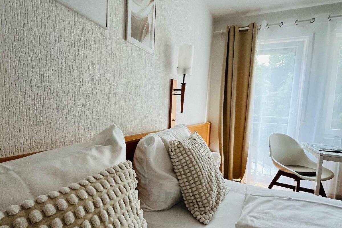 Une chambre d’hôtel avec un lit, un bureau, une chaise et une fenêtre avec des rideaux.