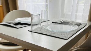 Een eettafel gedekt met helder glaswerk en borden, geplaatst nabij een raam met dunne gordijnen.