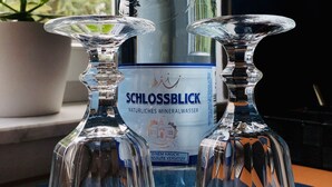Een fles SCHLOSSBLICK mineraalwater met twee glazen karafjes op een vensterbank.