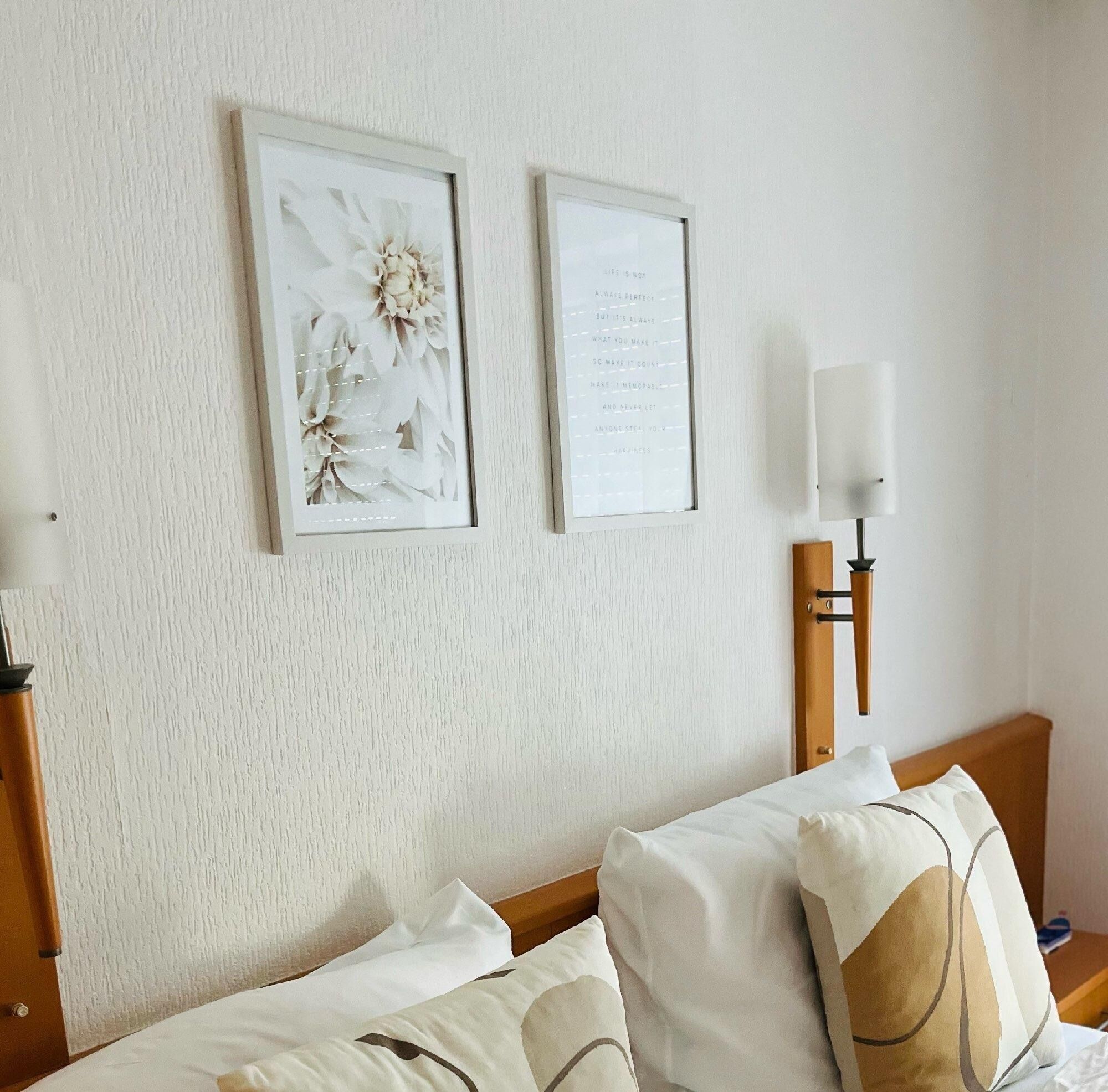 A hotel room with a bed, a nightstand, a lamp, and two framed pictures on the wall.