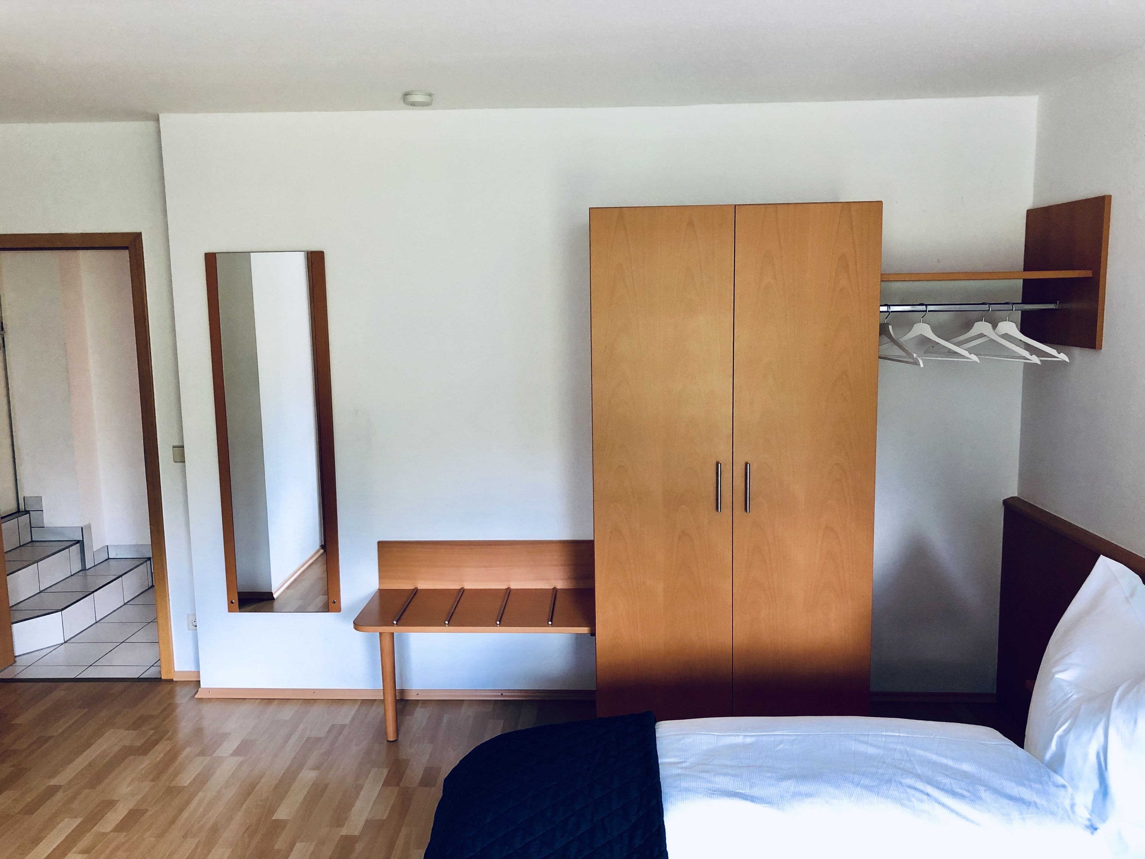 Un dormitorio con cama, armario de madera, banco y espejo.