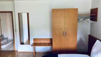 Un dormitorio con cama, armario de madera, banco y espejo.