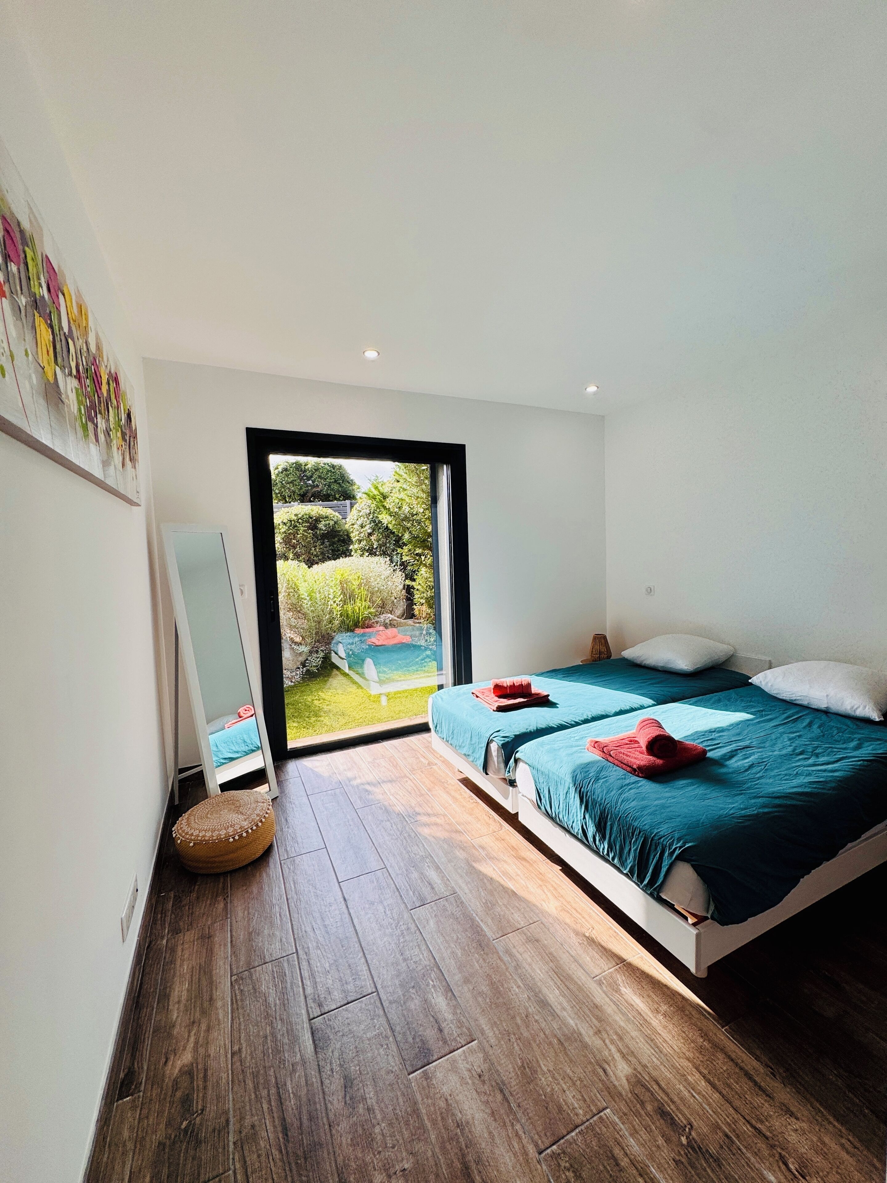 Ein modernes Schlafzimmer mit einem großen Bett, einer kleinen Sitzecke und Blick auf einen Garten durch eine Glastür.