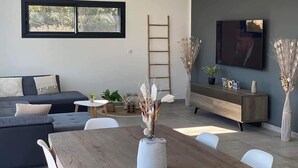 En moderne stue med en mørkegrå sofa, et træspisebord og et fjernsyn monteret på væggen.