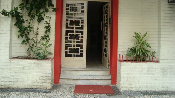 A building entrance with a red archway, a tiled floor, and potted plants on either side. - APART MARCELO - STUDIO COPACABANA (RIO DE JANEIRO)