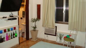 A room with a television on a shelf, a potted plant, a radiator, and a chair. - APART MARCELO - STUDIO COPACABANA (RIO DE JANEIRO)
