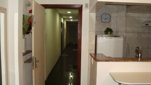A hotel hallway leading to a bathroom with a sink and a clock on the wall. - APART MARCELO - STUDIO COPACABANA (RIO DE JANEIRO)