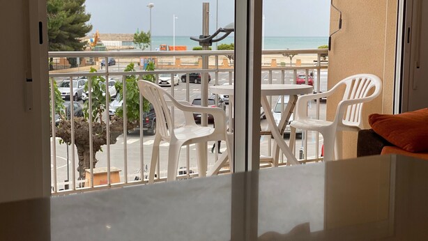 Un balcon avec des chaises et une table en plastique blanc, donnant sur un parking et une plage.