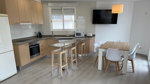 Une cuisine moderne avec des meubles en bois, un four encastré, un micro-ondes et un coin repas comprenant une table en bois et des chaises blanches.