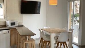 Une cuisine moderne équipée d’un téléviseur à écran plat, d’un four à micro-ondes et d’un lave-vaisselle Bosch. On y trouve une table à manger en bois, avec des chaises blanches et un tabouret en bois.