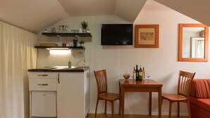 A compact kitchen with a refrigerator, sink, and wooden dining table with chairs. A flat-screen TV and framed artwork are on the wall. - Apartments Ivana Old Town - Standard Studio - APT3 (Dubrovnik)