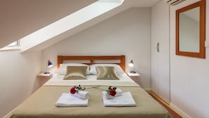 A hotel room with a sloped ceiling, a bed with two pillows, bedside lamps, a wardrobe, and a mirror. - Apartments Ivana Old Town - Standard Studio - APT3 (Dubrovnik)