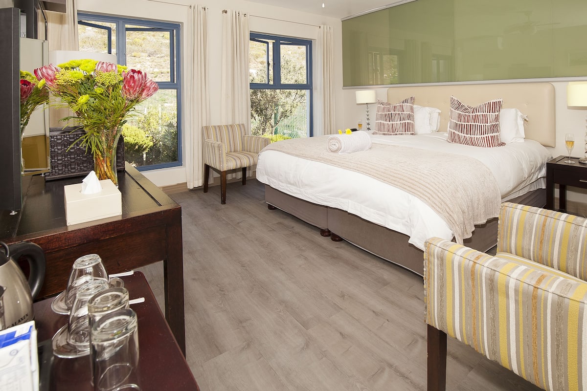 Habitación de hotel con cama, escritorio, silla, mesita de noche y ventana con cortinas.
