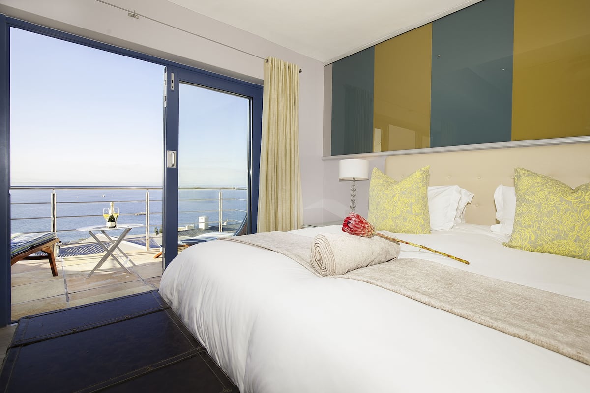 Una habitación de hotel con una cama grande, vistas al mar, un balcón con mesa y sillas, y un espejo amplio.