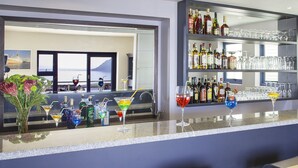 A bar area with a view of the sea, a variety of bottles and glasses, and a seating area with bar stools. - Magellans Hotel (Cape Town)