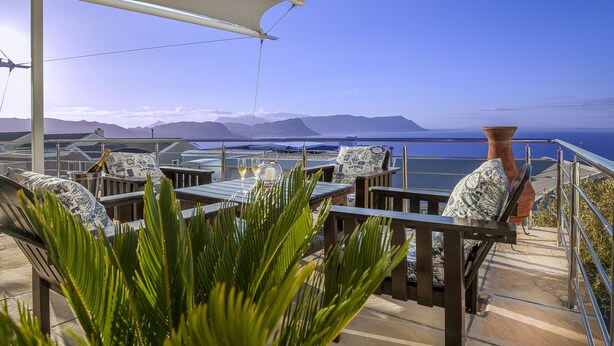 An outdoor seating area with tables and chairs, overlooking a body of water and mountains. - Magellans Hotel (Cape Town)