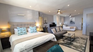 A modern hotel room with a large bed, a sofa, a desk, and a ceiling fan. - Magellans Hotel (Cape Town)