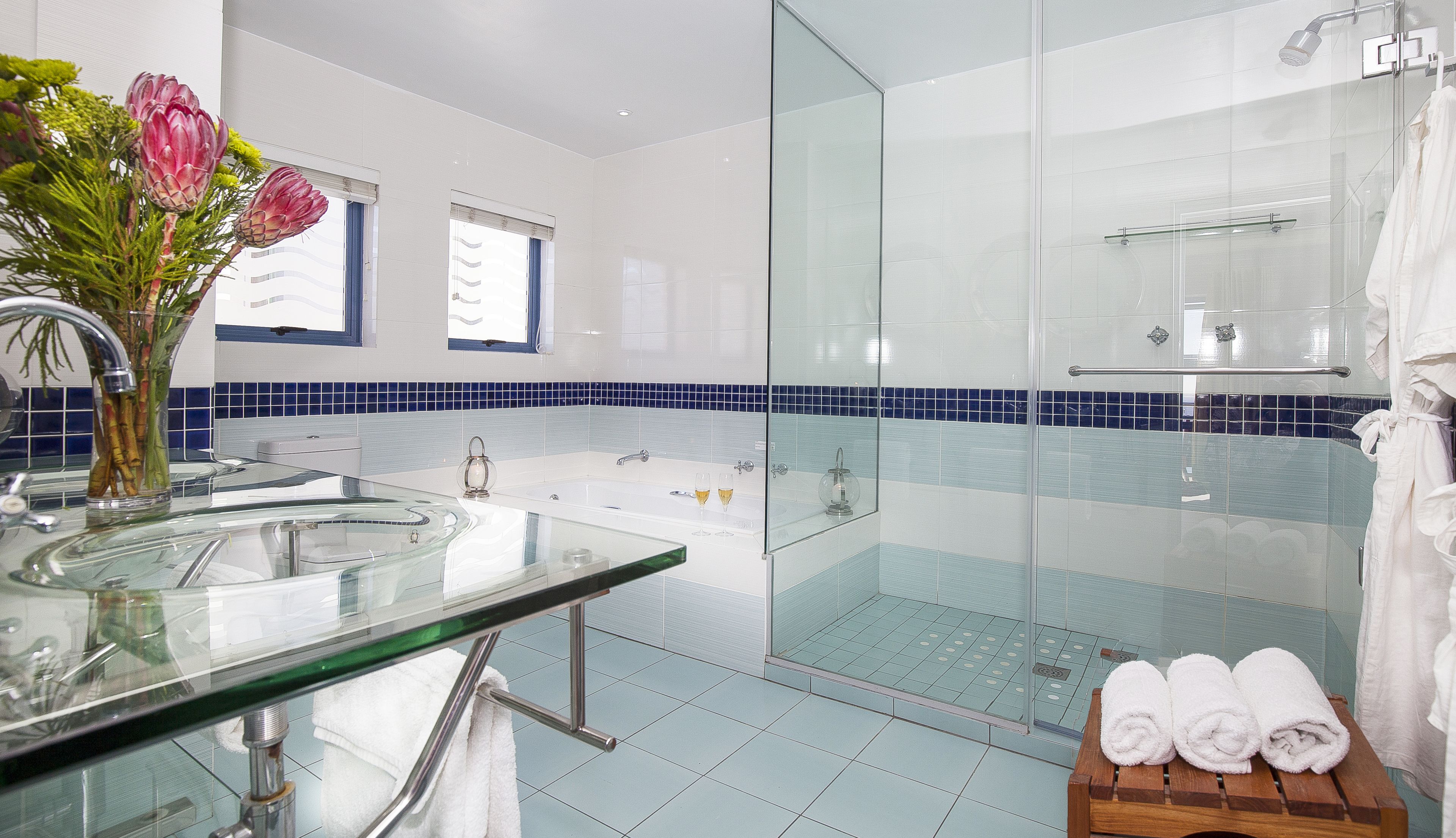 Un baño moderno con cabina de ducha de vidrio, dos lavamanos y tocador de vidrio.
