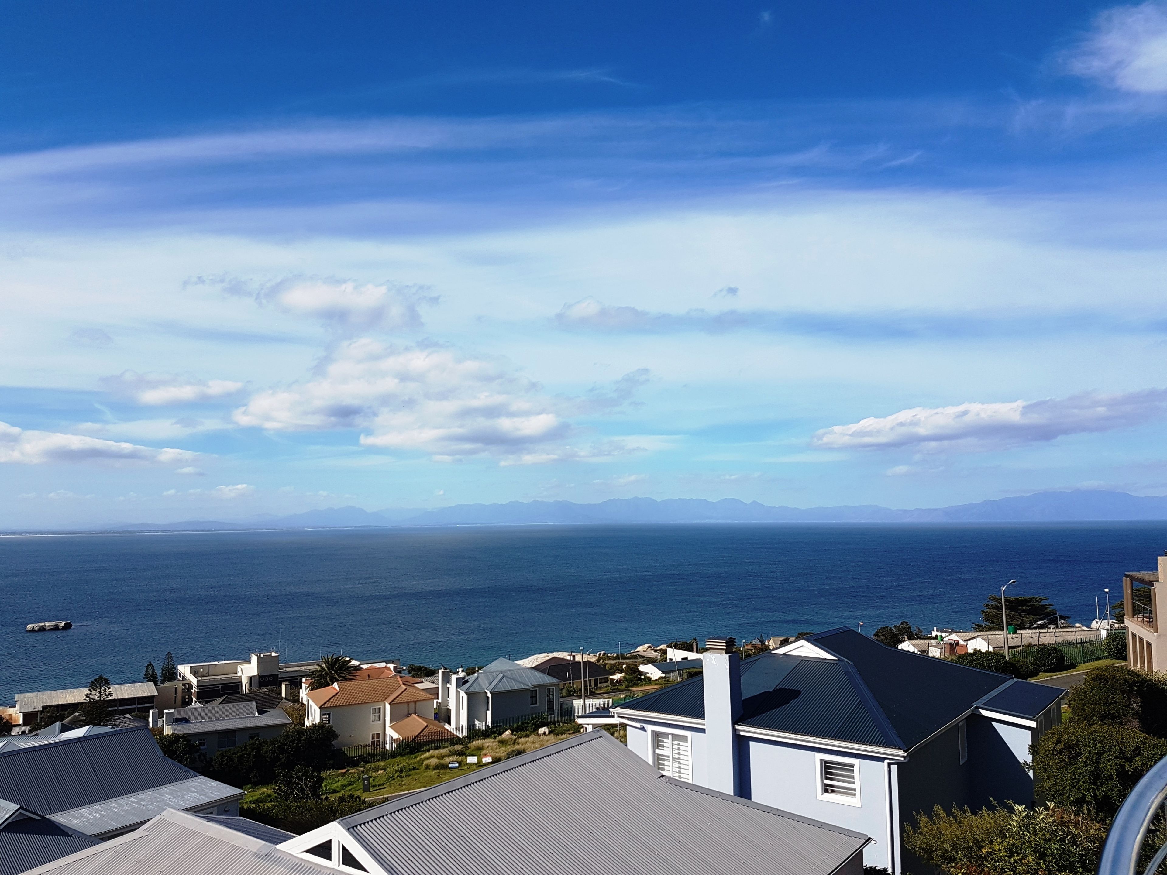 A coastal residential area with houses and a view of the sea and distant mountains.