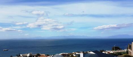 A coastal residential area with houses and a view of the sea and distant mountains.