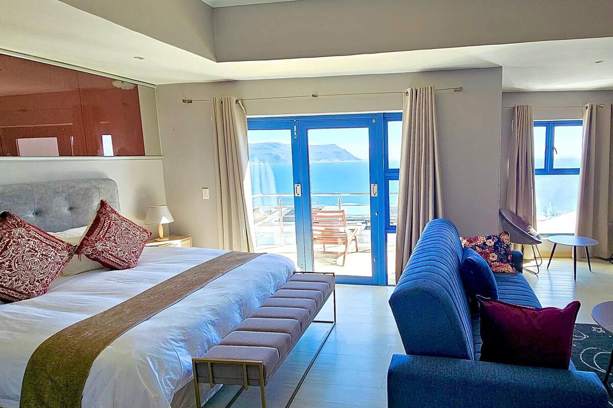 Habitación de hotel con una cama grande, un sofá, una mesita y un balcón con vista al mar.