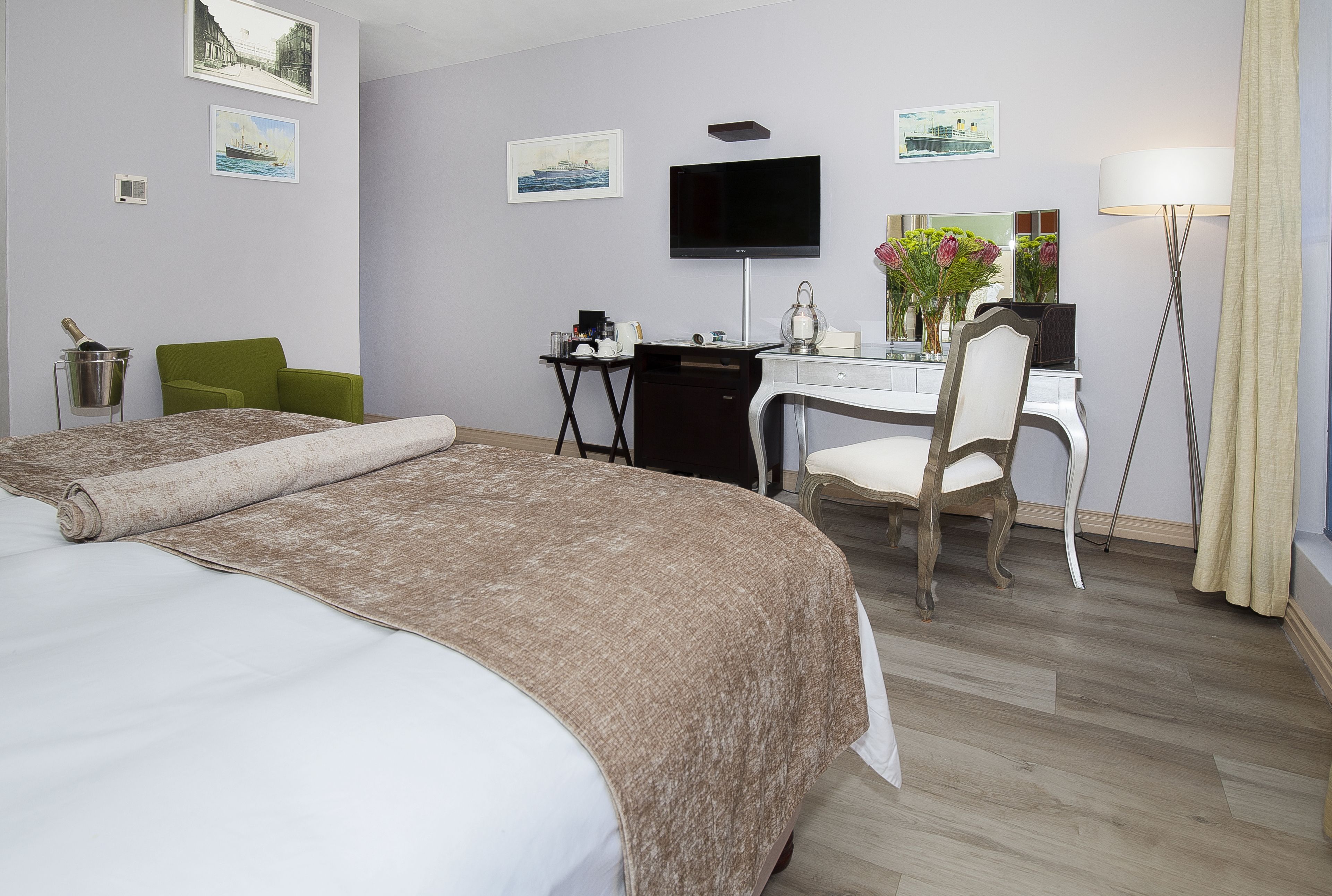 Habitación de hotel con dos camas, un escritorio, una silla, un televisor y obras de arte en las paredes.