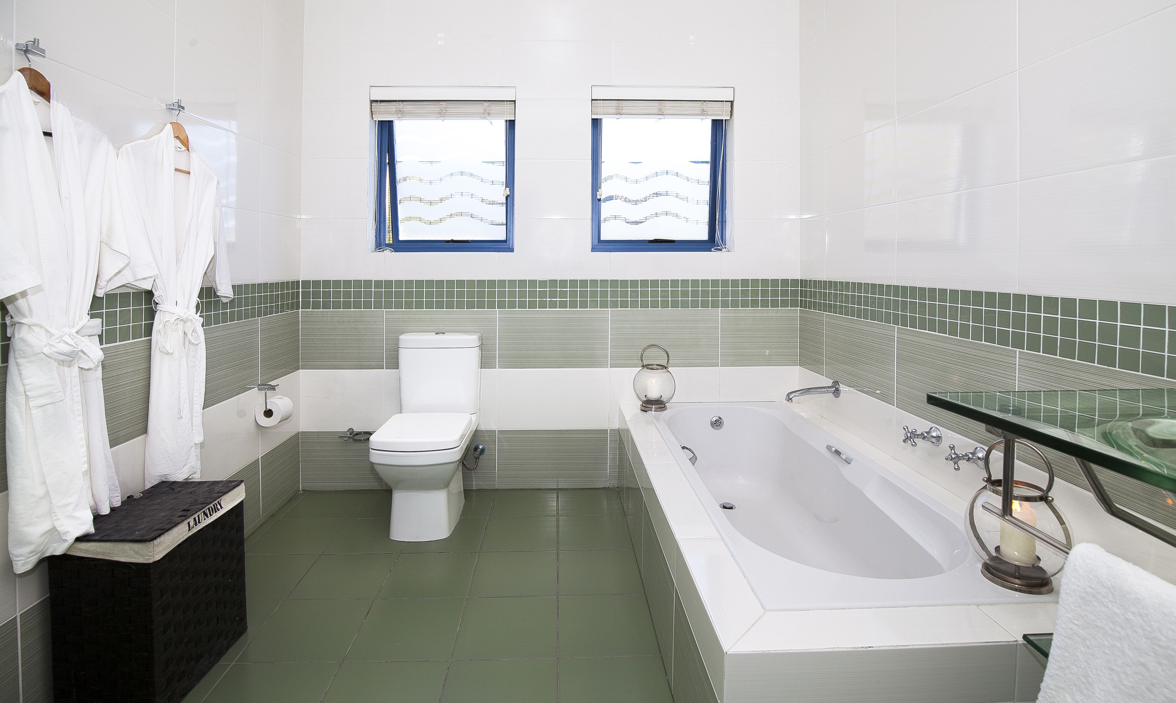 A bathroom with a toilet, bathtub, and two windows with blue curtains.