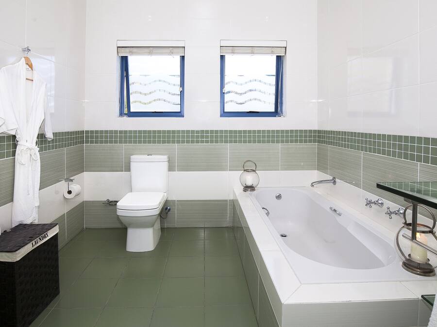 A bathroom with a toilet, bathtub, and two windows with blue curtains.