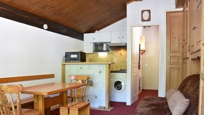 Een kleine keuken met een wasmachine, een magnetron en een eethoek met een houten tafel en stoelen.