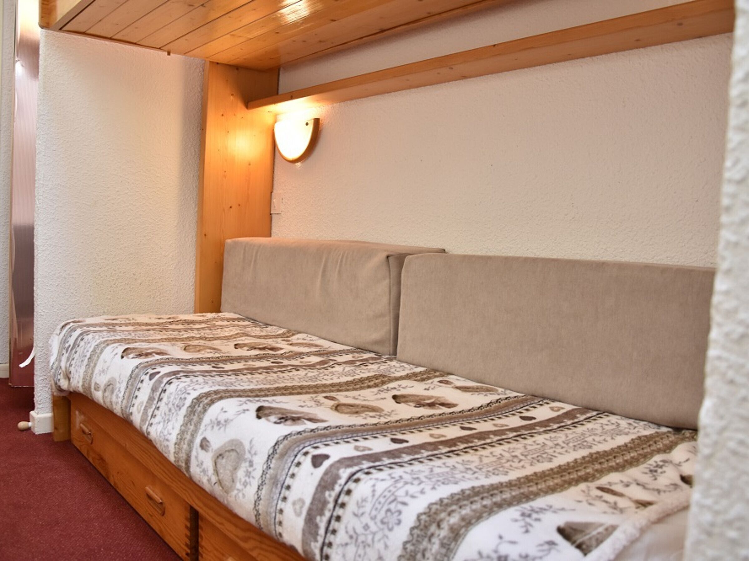 Una cama individual con una colcha estampada en una habitación con vigas de madera y un aplique de pared.