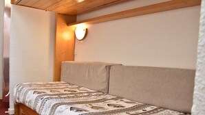 Een eenpersoonsbed met een bedspread met patroon in een kamer met houten balken en een wandlamp.