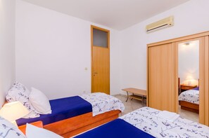 Un dormitorio con dos camas, un armario de madera, un escritorio y un equipo de aire acondicionado.