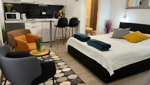 A modern hotel room with a bed, two chairs, a small table with a vase, a kitchen area, and a bathroom visible through an open door. - Apartments Noa Old Town - Studio - First Floor (Dubrovnik)