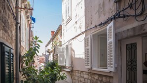 A narrow street with stone buildings, white shutters, and a tree in the foreground. - Apartments Noa Old Town - Studio - First Floor (Dubrovnik)