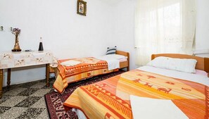 Una habitación con dos camas, una mesita con un florero y una ventana con cortinas.