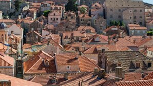 Uma área urbana densamente povoada, com edifícios de pedra bem próximos e telhados de telha vermelha.
