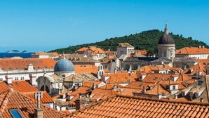 Paisagem costeira com edifícios de telhados em terracota, uma cúpula imponente e uma colina ao fundo.
